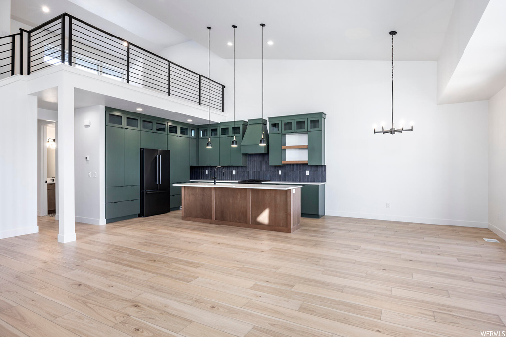 Kitchen featuring custom range hood, pendant lighting, a kitchen island with sink, black refrigerator, and a towering ceiling