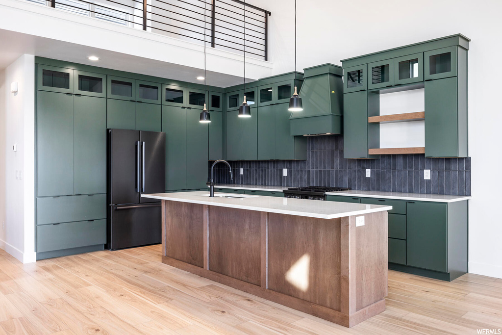 Kitchen with green cabinets, custom exhaust hood, an island with sink, and black fridge