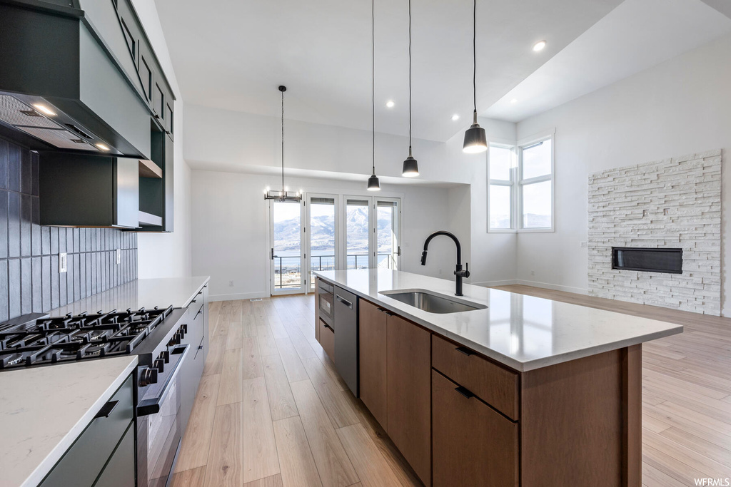 Kitchen featuring sink, range with gas cooktop, a center island with sink, hanging light fixtures, and wall chimney exhaust hood