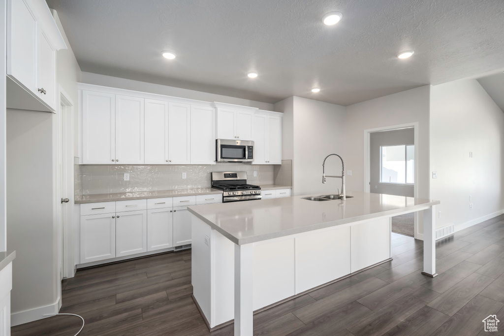 Kitchen featuring dark hardwood / wood-style flooring, appliances with stainless steel finishes, an island with sink, backsplash, and sink