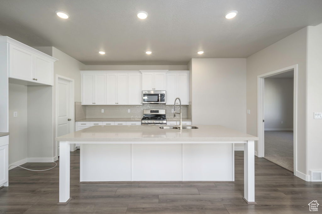 Kitchen featuring dark hardwood / wood-style floors, stainless steel appliances, a center island with sink, and sink