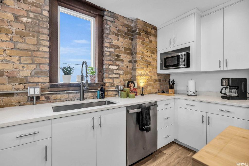 Kitchen featuring sink, light hardwood / wood-style flooring, stainless steel appliances, brick wall, and white cabinetry