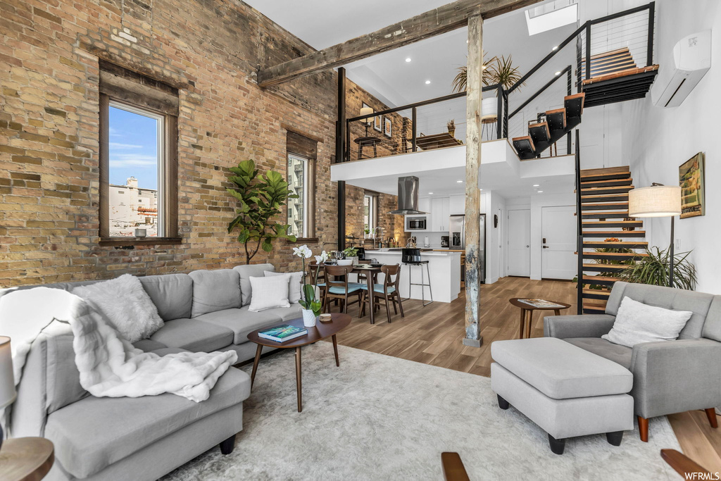 Living room with a wall unit AC, a towering ceiling, light hardwood / wood-style floors, and brick wall