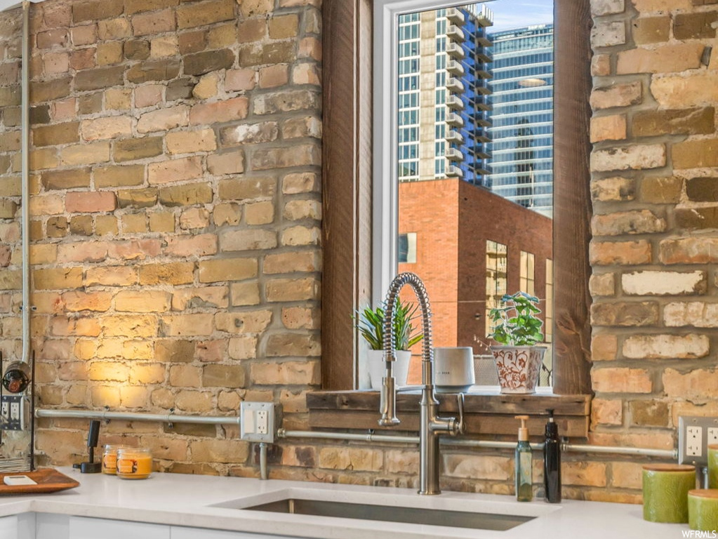 Kitchen featuring sink, brick wall, dishwasher, and white cabinetry