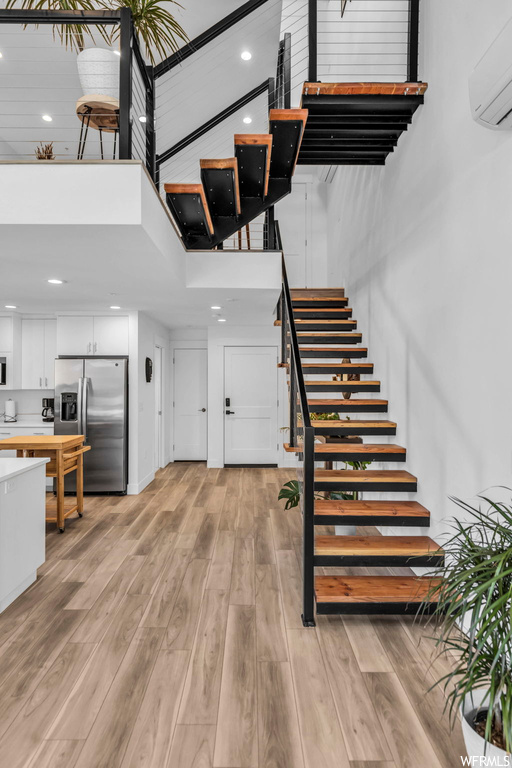 Stairs with a wall mounted AC, light hardwood / wood-style floors, and a towering ceiling