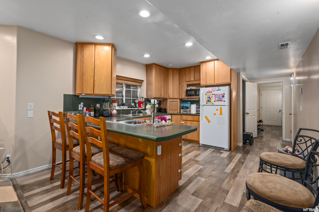 Kitchen featuring white refrigerator, dark hardwood / wood-style floors, a breakfast bar area, and kitchen peninsula