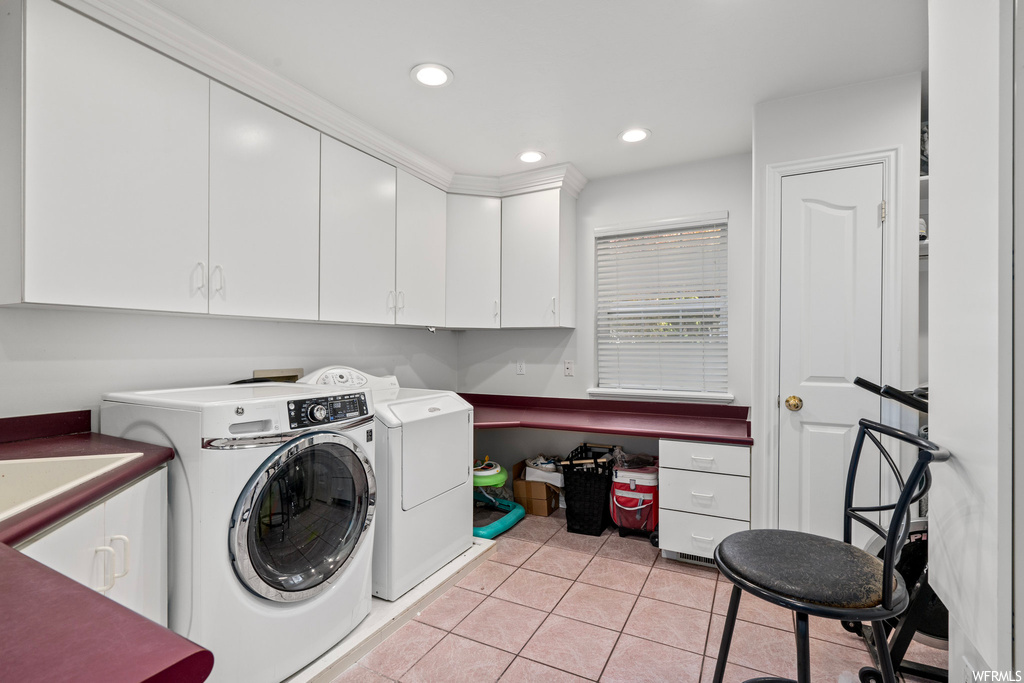 Clothes washing area featuring washing machine and clothes dryer, sink, cabinets, and light tile flooring
