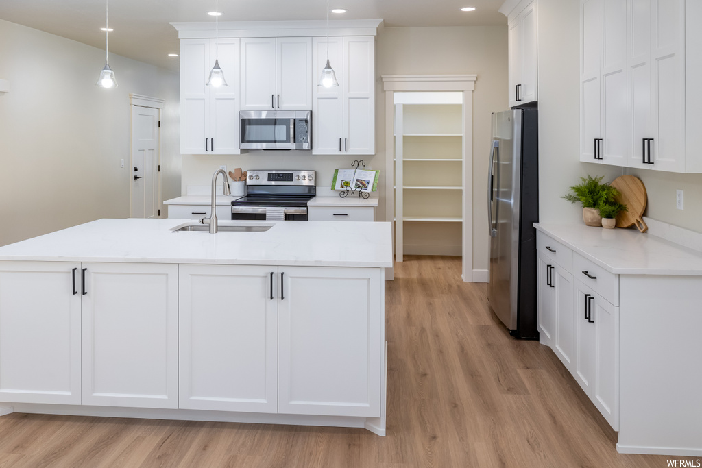 Kitchen with a kitchen island with sink, appliances with stainless steel finishes, light hardwood / wood-style floors, white cabinets, and decorative light fixtures