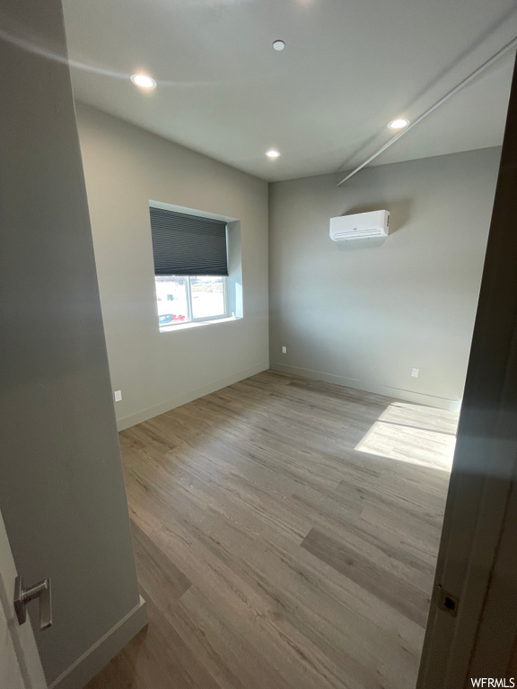 Empty room with a wall unit AC and light hardwood / wood-style flooring