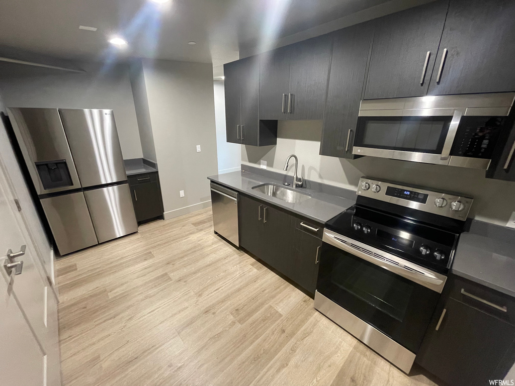 Kitchen with light hardwood / wood-style floors, sink, and appliances with stainless steel finishes