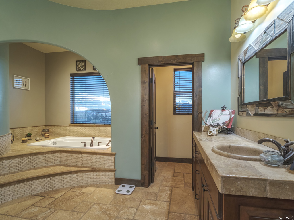 Bathroom featuring tile floors, plenty of natural light, vanity with extensive cabinet space, and tiled tub