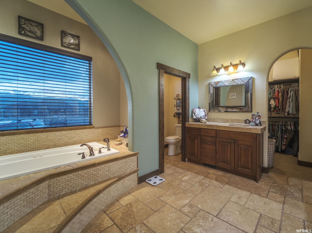 Bathroom with tile flooring, toilet, vanity with extensive cabinet space, and tiled tub