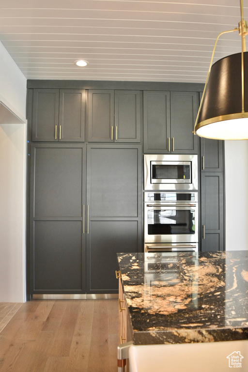 Kitchen with dark stone countertops, gray cabinetry, appliances with stainless steel finishes, and light hardwood / wood-style floors