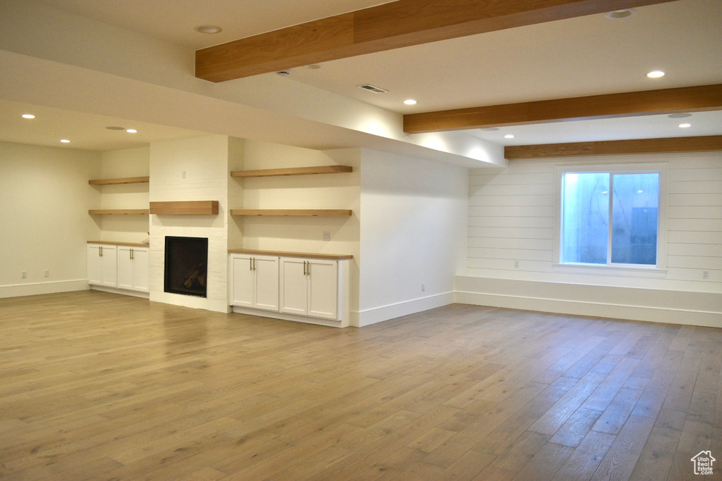 Unfurnished living room featuring light hardwood / wood-style flooring, a large fireplace, and beam ceiling