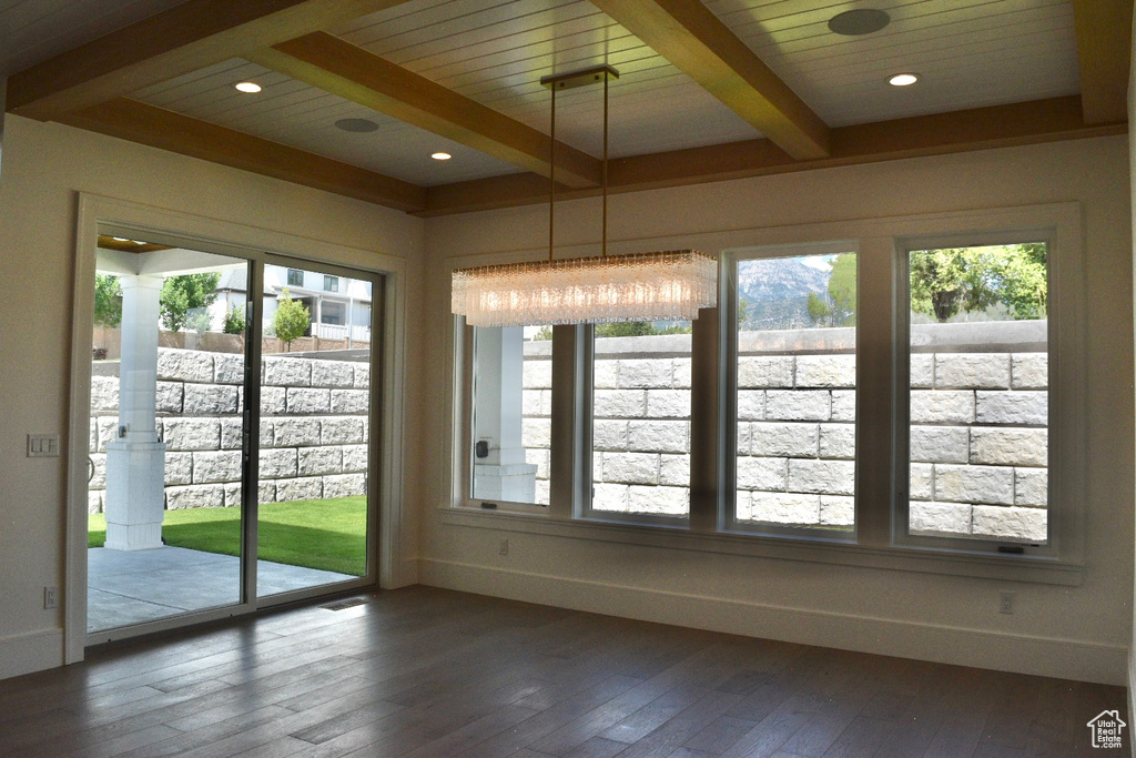 Unfurnished dining area with beam ceiling, a wealth of natural light, and dark wood-type flooring