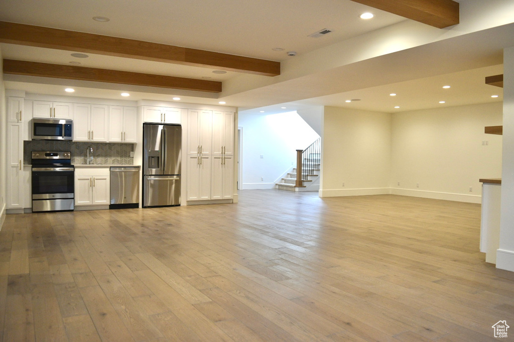 Kitchen with light hardwood / wood-style flooring, beam ceiling, white cabinets, and stainless steel appliances