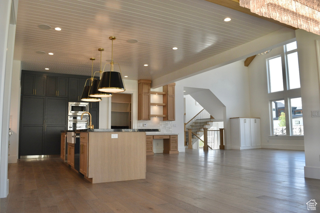 Kitchen with backsplash, hardwood / wood-style flooring, a center island with sink, and stainless steel appliances