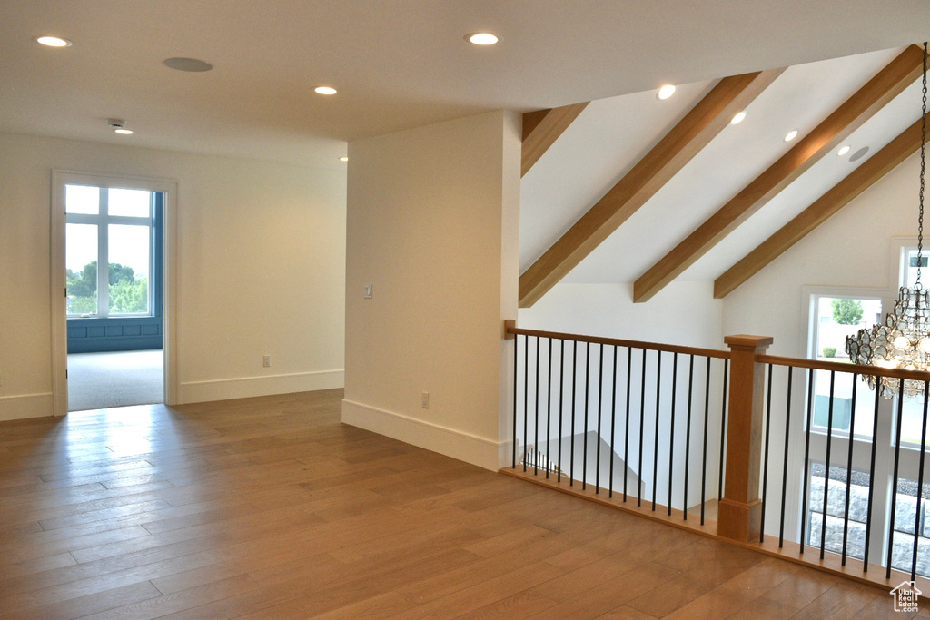 Spare room featuring hardwood / wood-style flooring, a healthy amount of sunlight, vaulted ceiling with beams, and a chandelier