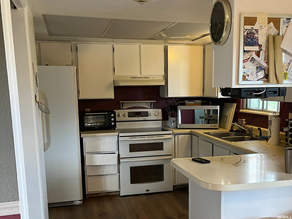 Kitchen with sink, white appliances, a kitchen breakfast bar, dark hardwood / wood-style floors, and kitchen peninsula