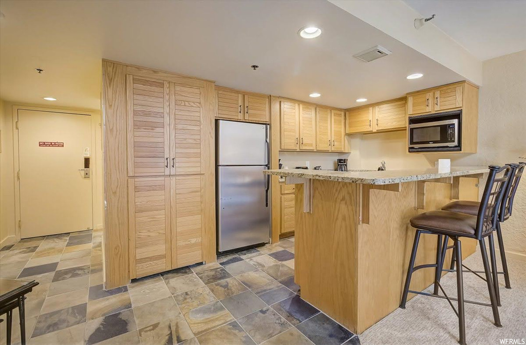 Kitchen with a breakfast bar, light tile floors, light brown cabinets, and appliances with stainless steel finishes