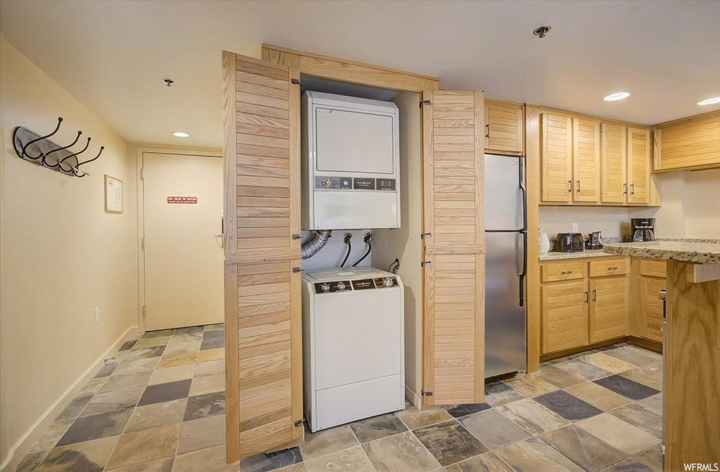 Kitchen featuring stacked washer / dryer, water heater, stainless steel fridge, light tile floors, and light brown cabinetry