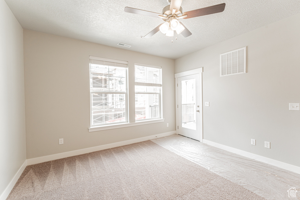 Carpeted empty room with ceiling fan, a healthy amount of sunlight, and a textured ceiling