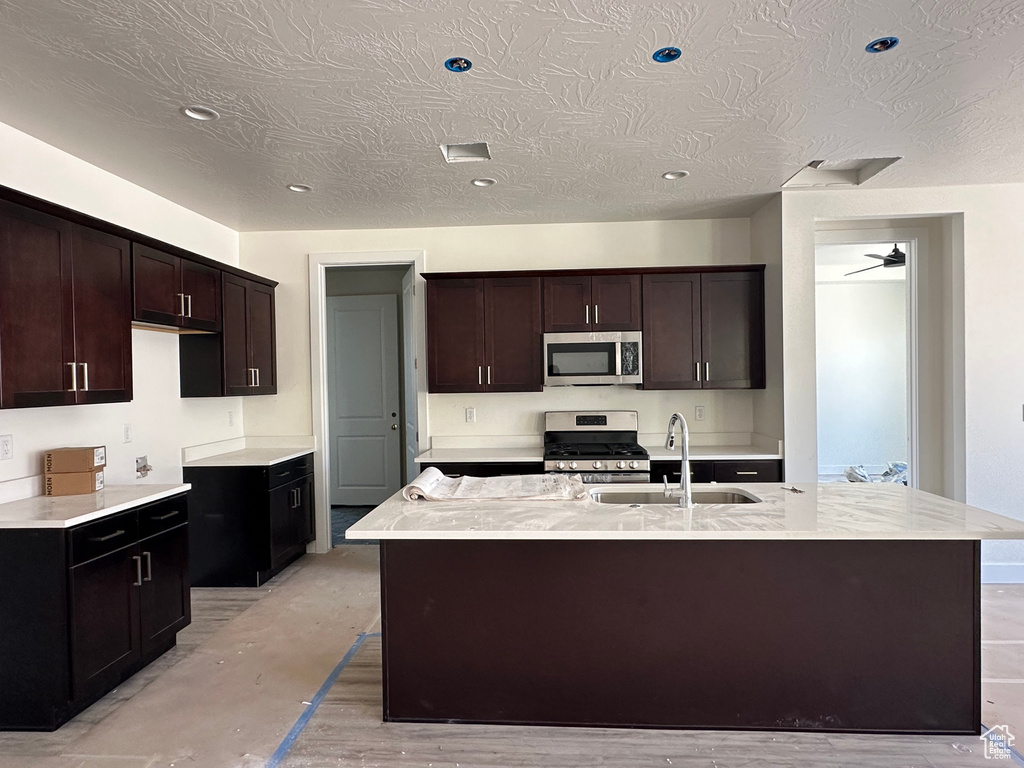 Kitchen with a center island with sink, stainless steel appliances, dark brown cabinetry, sink, and ceiling fan