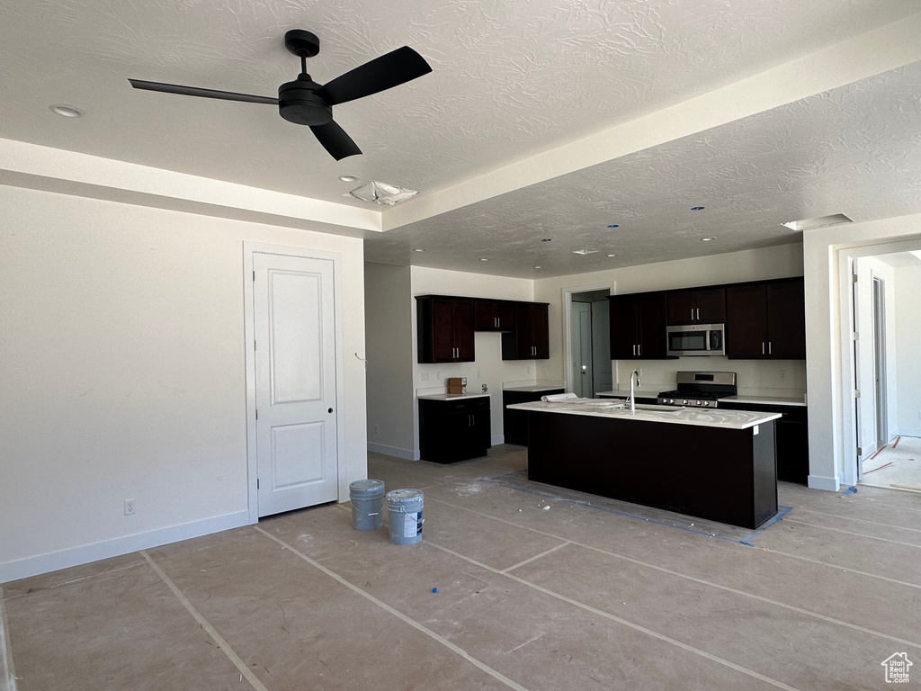 Kitchen with appliances with stainless steel finishes, a kitchen island with sink, dark brown cabinetry, sink, and ceiling fan