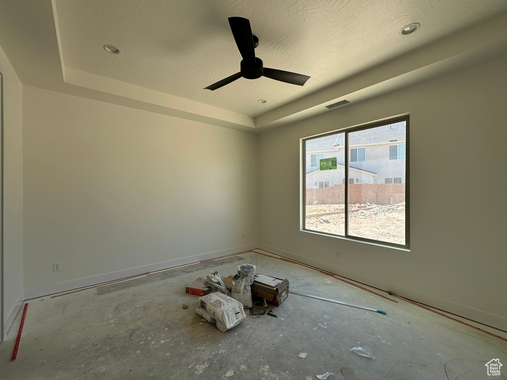 Spare room with ceiling fan, concrete floors, a tray ceiling, and a textured ceiling