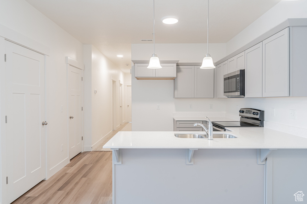 Kitchen featuring sink, hanging light fixtures, stainless steel appliances, light hardwood / wood-style flooring, and kitchen peninsula