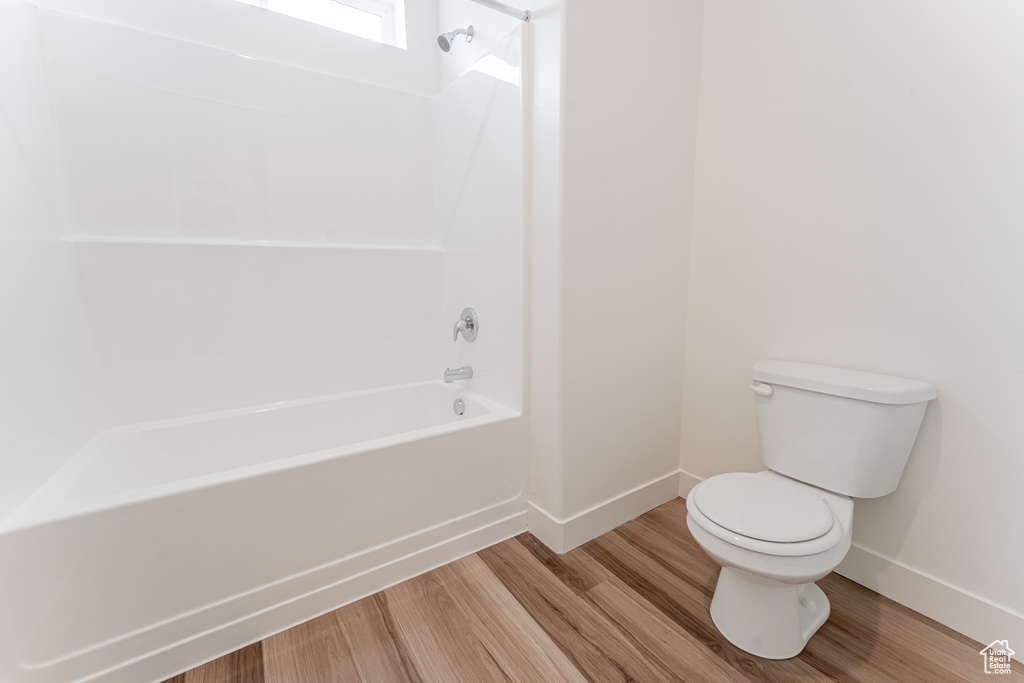 Bathroom with hardwood / wood-style floors, shower / tub combination, and toilet
