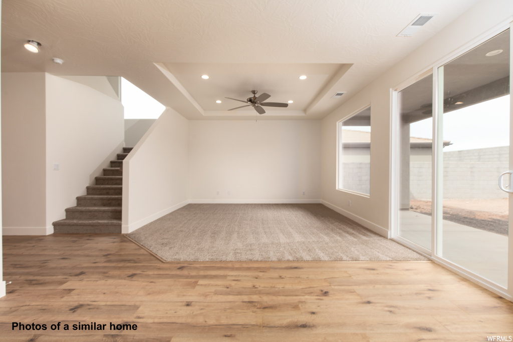 Unfurnished room with a tray ceiling, light wood-type flooring, and ceiling fan