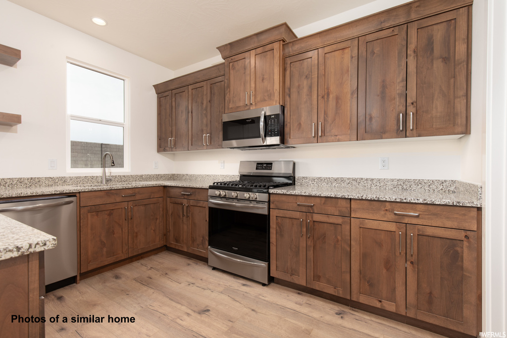 Kitchen featuring light hardwood / wood-style flooring, sink, stainless steel appliances, and light stone counters