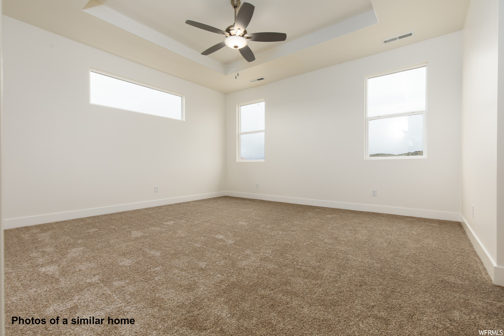 Carpeted empty room featuring ceiling fan and a tray ceiling