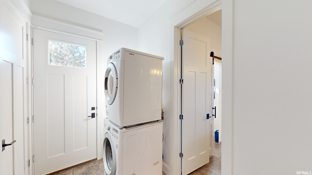 Laundry area featuring light tile flooring and stacked washing maching and dryer