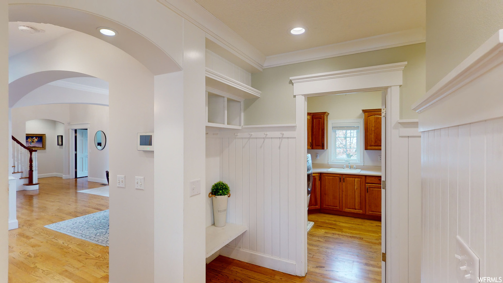 Corridor with ornamental molding, sink, and light hardwood / wood-style floors