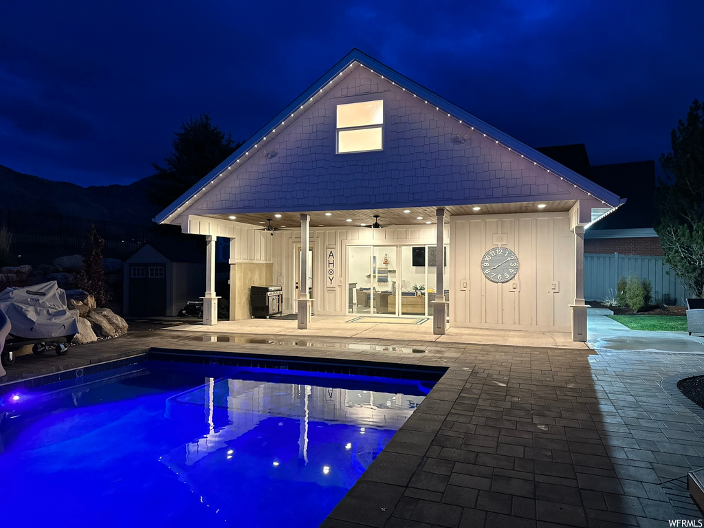 Pool at night with ceiling fan, a patio, and a storage shed