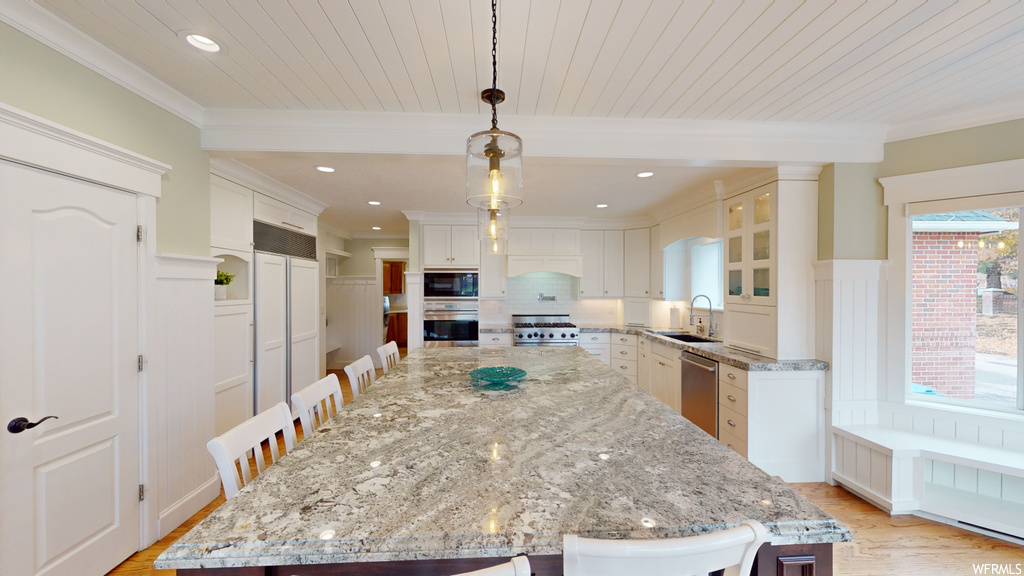 Kitchen with built in appliances, a center island, white cabinets, and light hardwood / wood-style floors