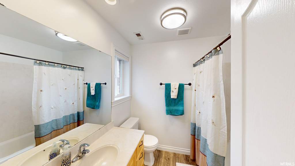 Full bathroom with toilet, shower / tub combo, hardwood / wood-style flooring, and vanity