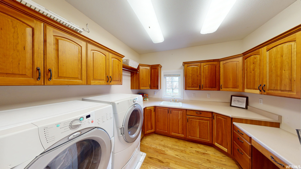 Clothes washing area with cabinets, separate washer and dryer, sink, and light hardwood / wood-style floors