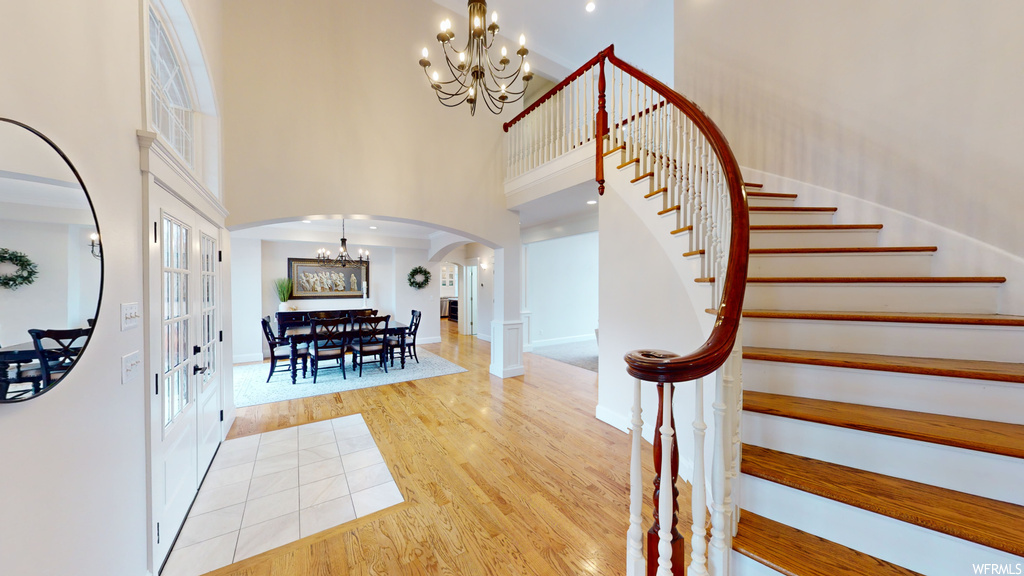 Stairs featuring a chandelier, a towering ceiling, and light hardwood / wood-style floors