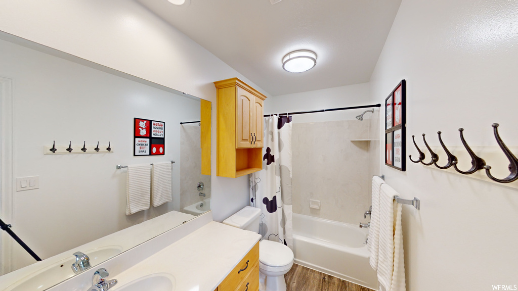 Full bathroom with toilet, shower / bath combo with shower curtain, wood-type flooring, and vanity