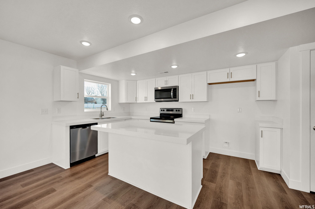 Kitchen with dark wood-type flooring, white cabinets, a kitchen island, and appliances with stainless steel finishes