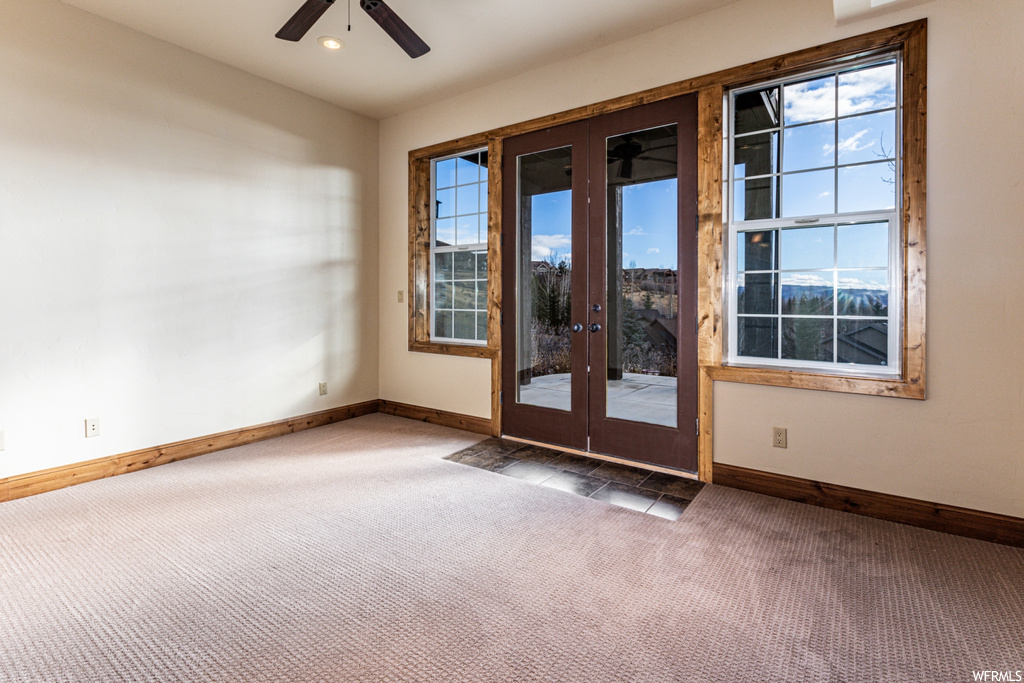 Unfurnished room with french doors, dark carpet, ceiling fan, and a healthy amount of sunlight