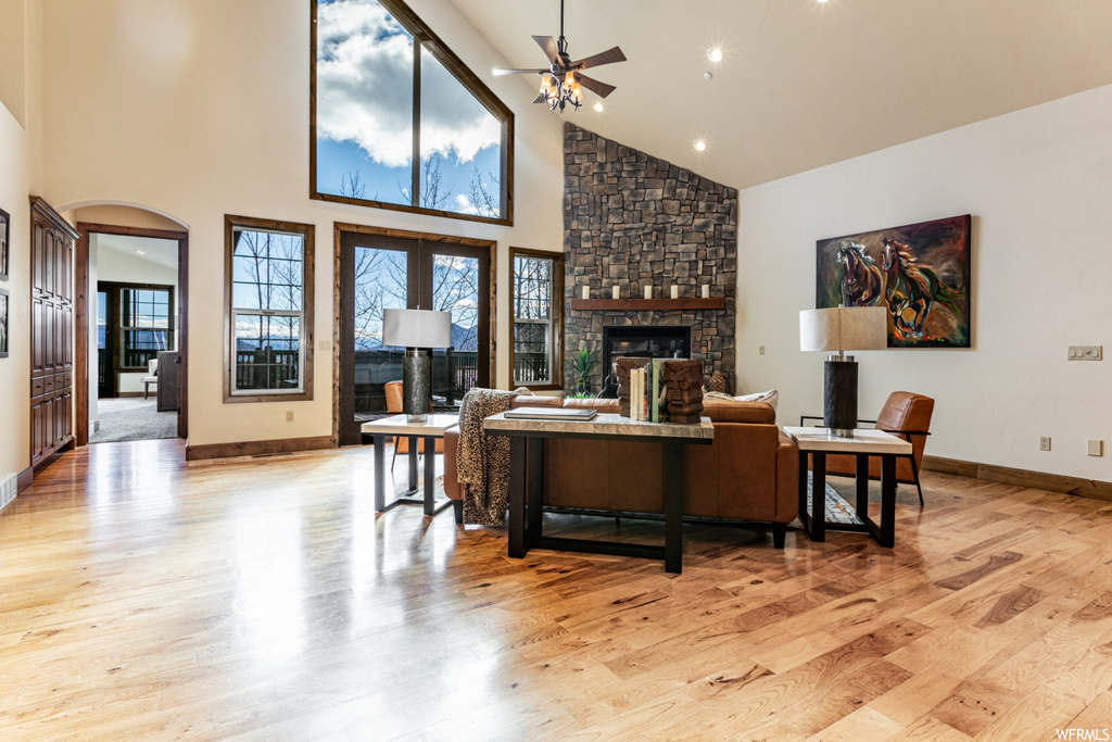 Living room featuring light hardwood / wood-style flooring, ceiling fan, a fireplace, and high vaulted ceiling