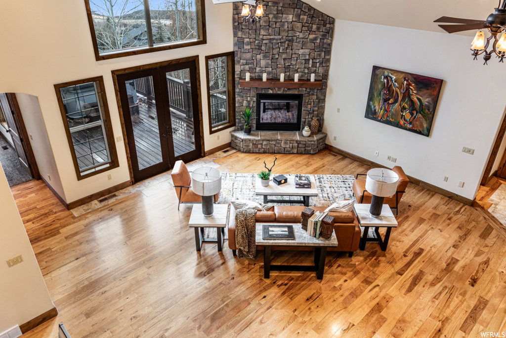 Living room featuring light hardwood / wood-style flooring, ceiling fan, a stone fireplace, and high vaulted ceiling