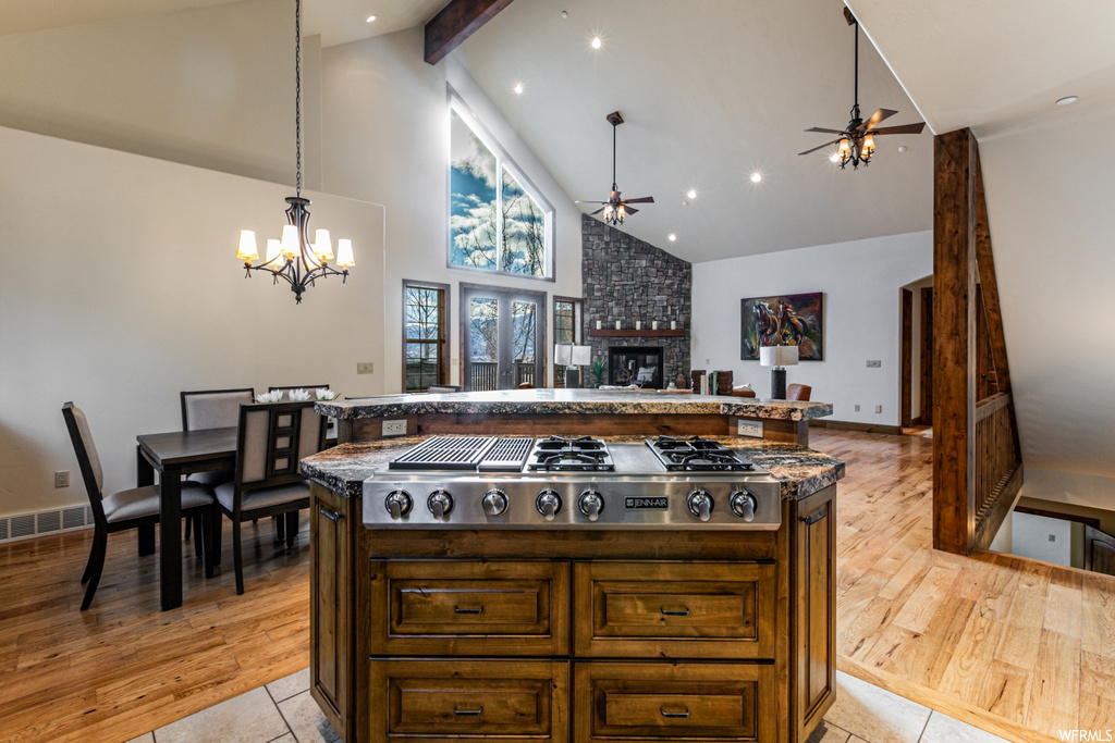 Kitchen with a center island, ceiling fan with notable chandelier, light hardwood / wood-style floors, a stone fireplace, and beamed ceiling