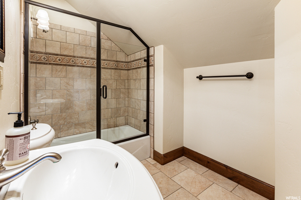 Full bathroom with sink, vaulted ceiling, bath / shower combo with glass door, toilet, and tile floors