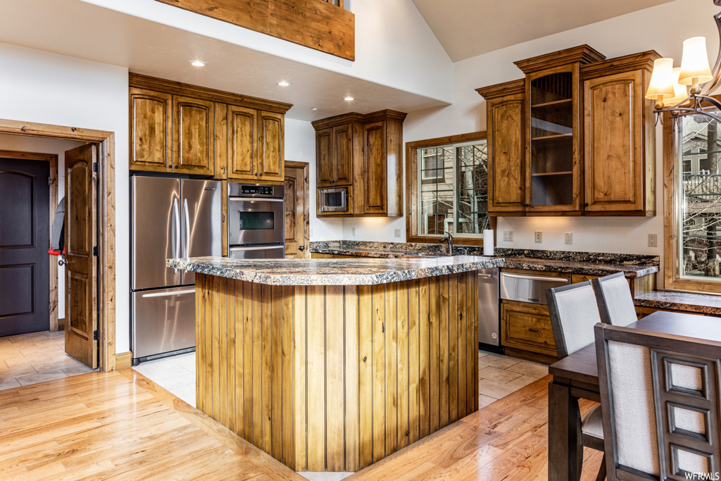 Kitchen featuring high vaulted ceiling, appliances with stainless steel finishes, a chandelier, light hardwood / wood-style flooring, and a kitchen island