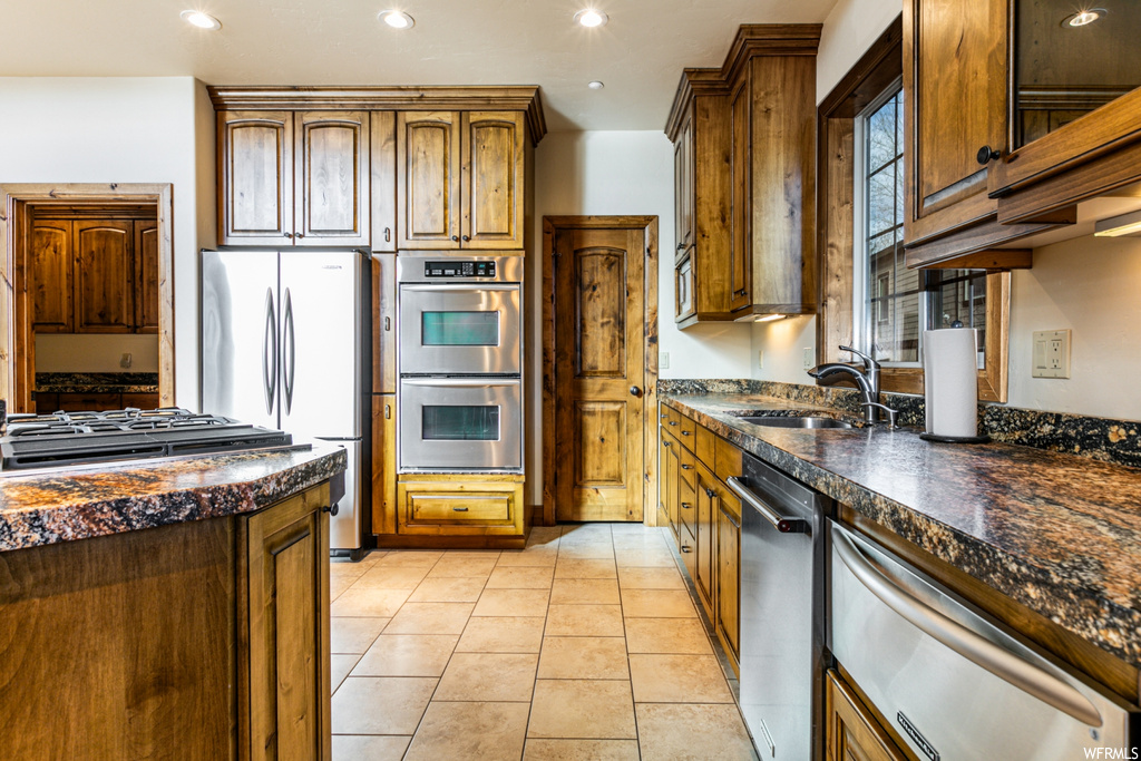 Kitchen featuring dark stone countertops, light tile flooring, sink, and appliances with stainless steel finishes
